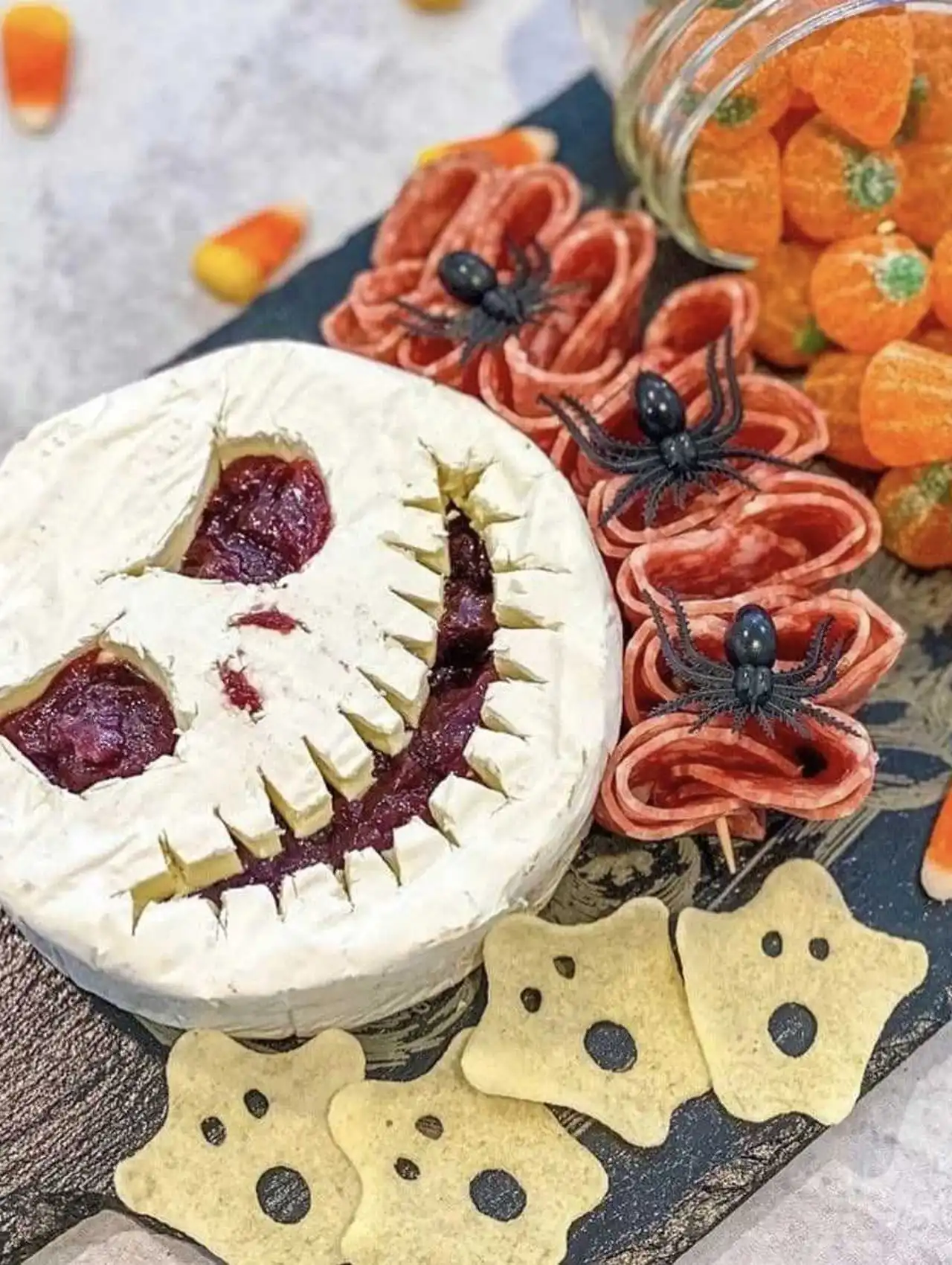 Jack Skellington halloween charcuterie board with brie cheese face, candy pumpkins, and salami roses.