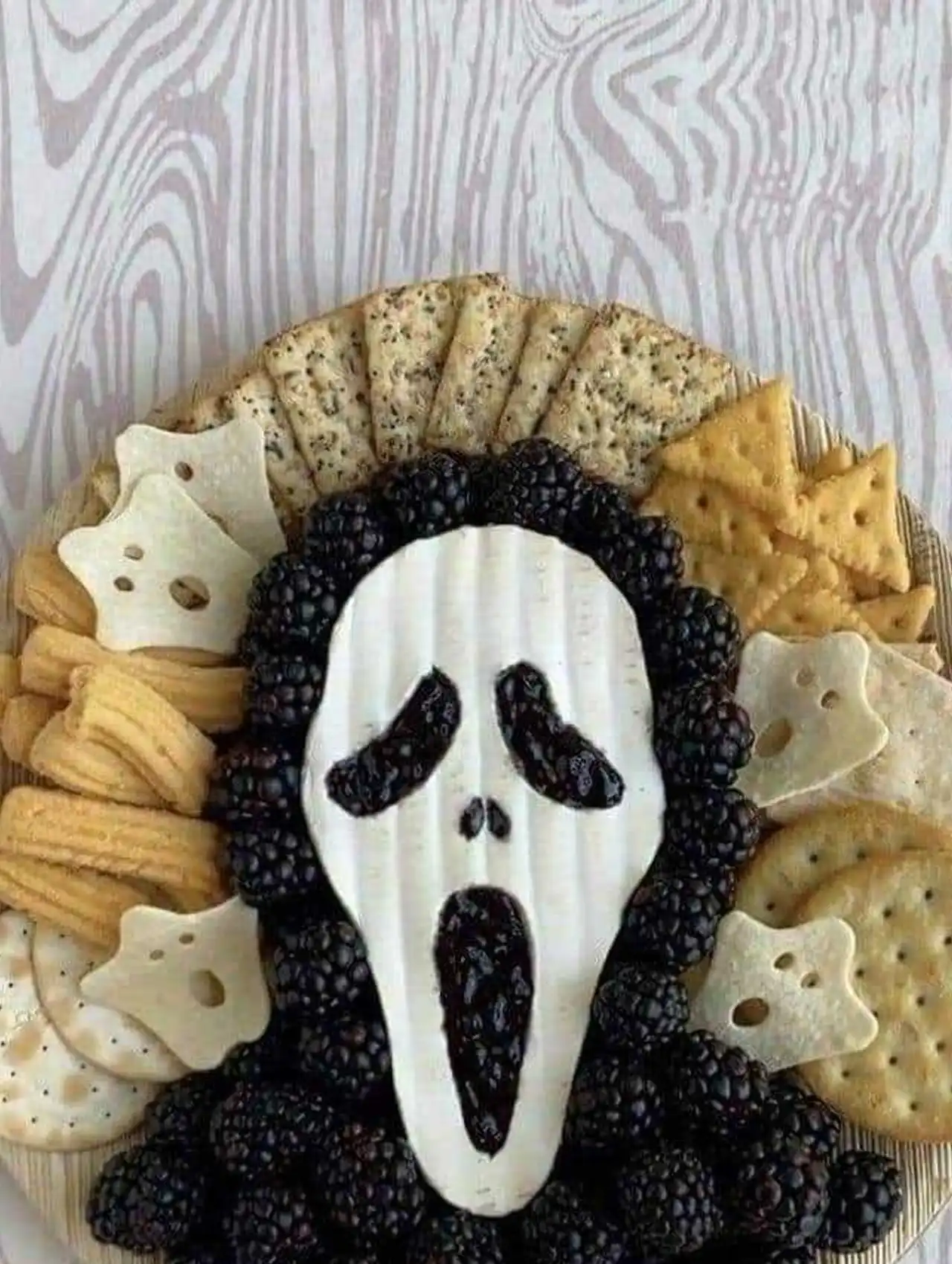Scream halloween charcuterie board with blackberries, cheese mask, and assorted crackers.