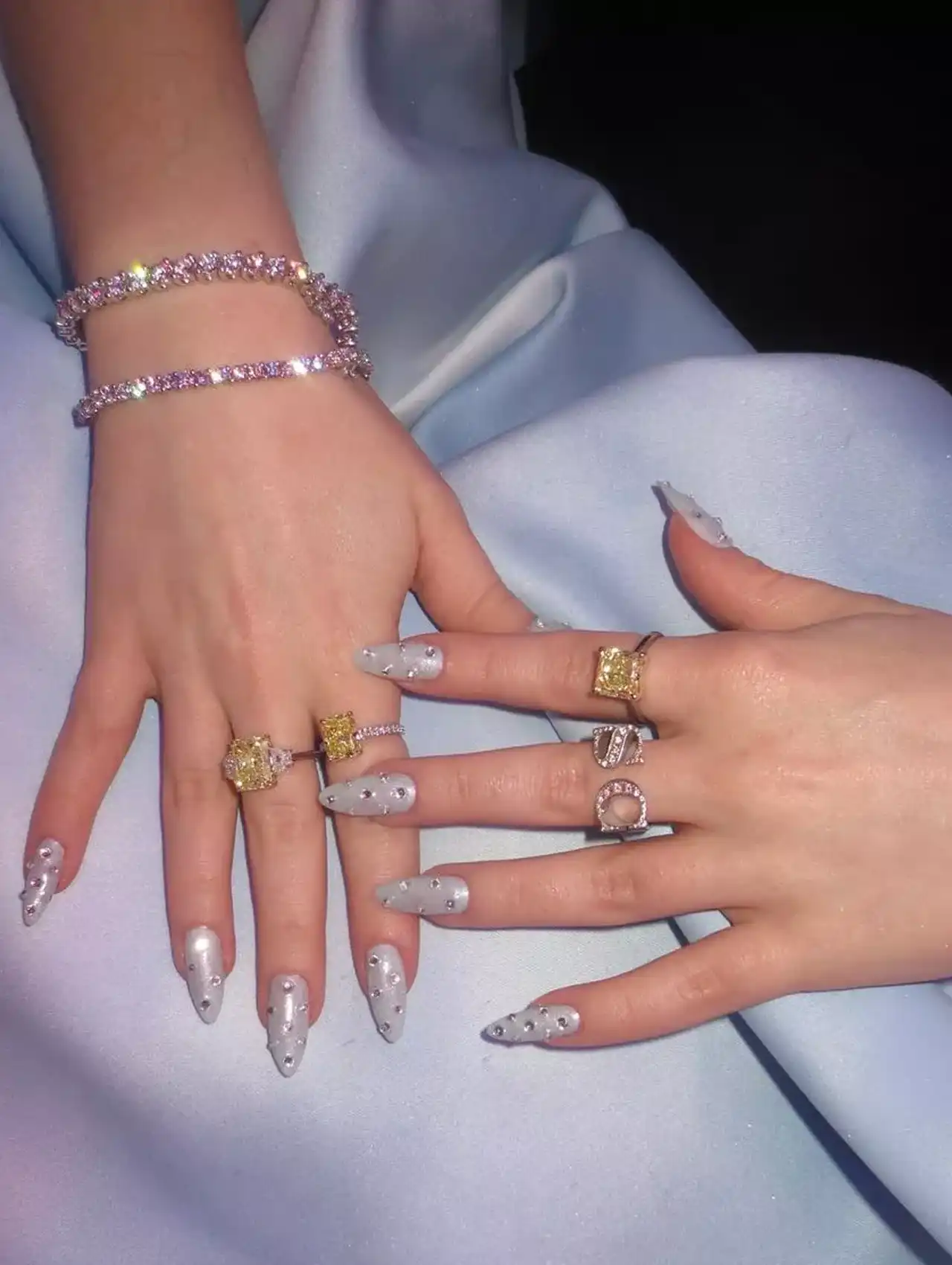 Sabrina Carpenter with frosty silver celebrity nails and diamond rings on a blue satin background