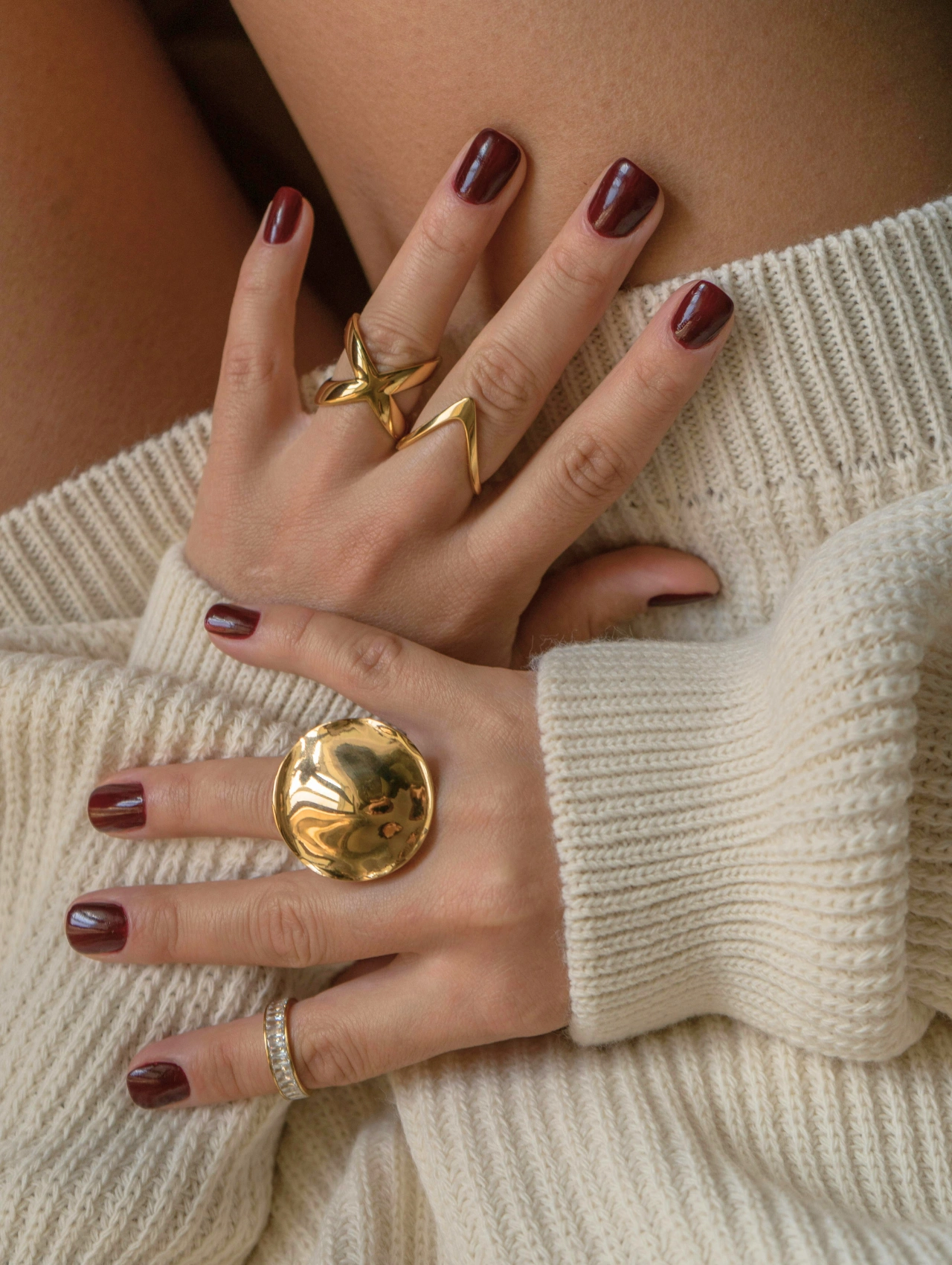 Manos con uñas en tendencia otoño con esmalte color vino y anillos dorados, mostrando un look elegante y cálido para la temporada.