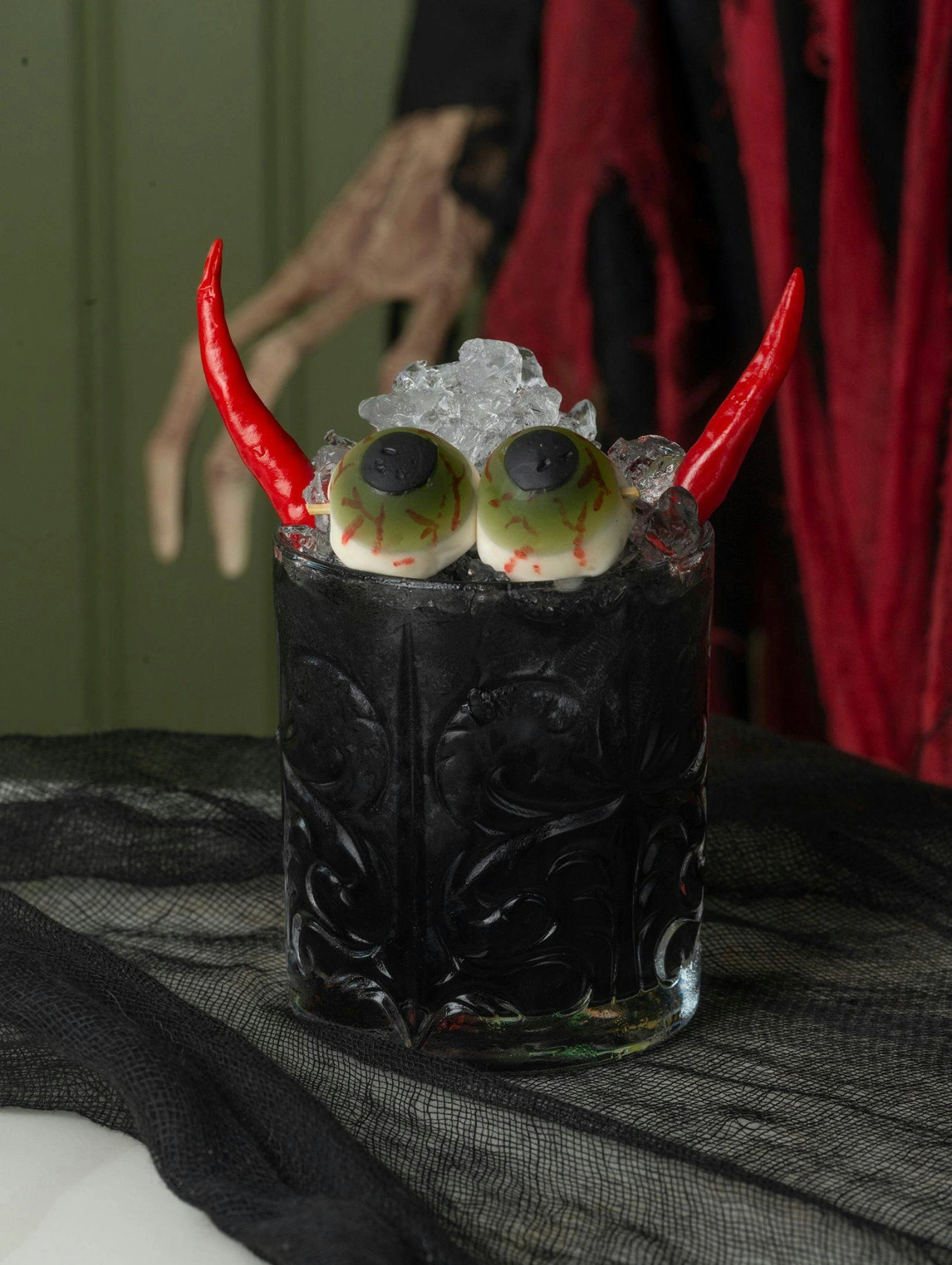 Cóctel negro decorado con ojos comestibles y cuernos rojos, un diseño creativo inspirado en Halloween.
