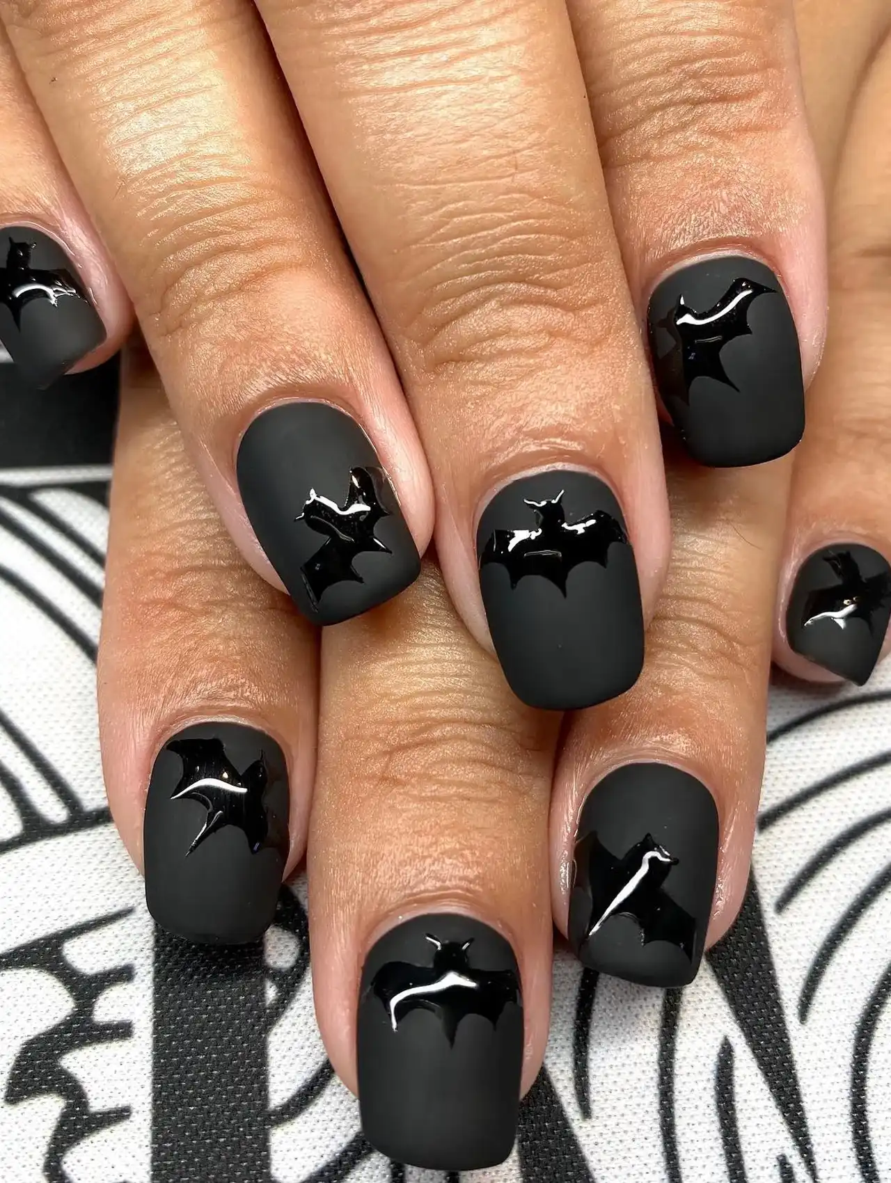 Minimalistic Halloween nails with matte black base and glossy black bat accents.