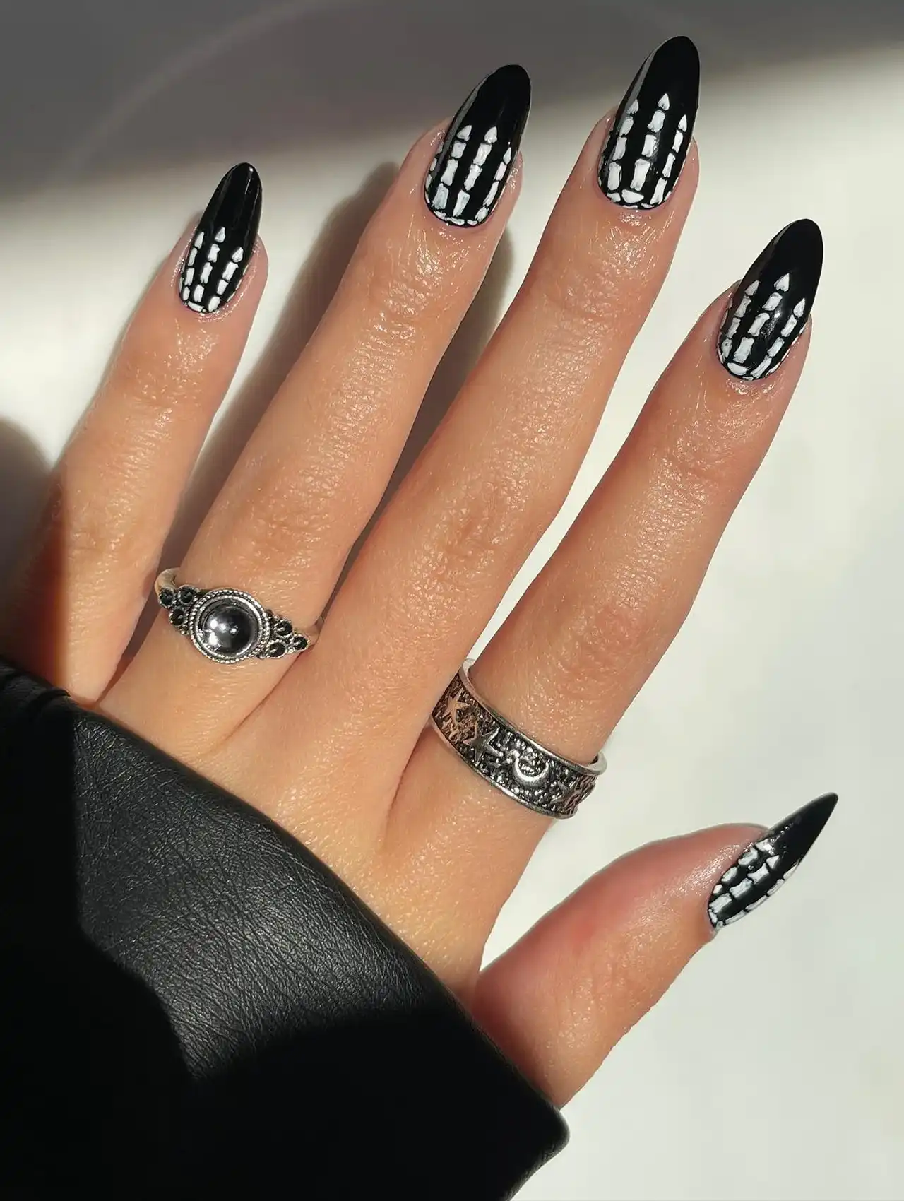 Minimalistic Halloween nails with black polish and tiny white skeleton bone designs.