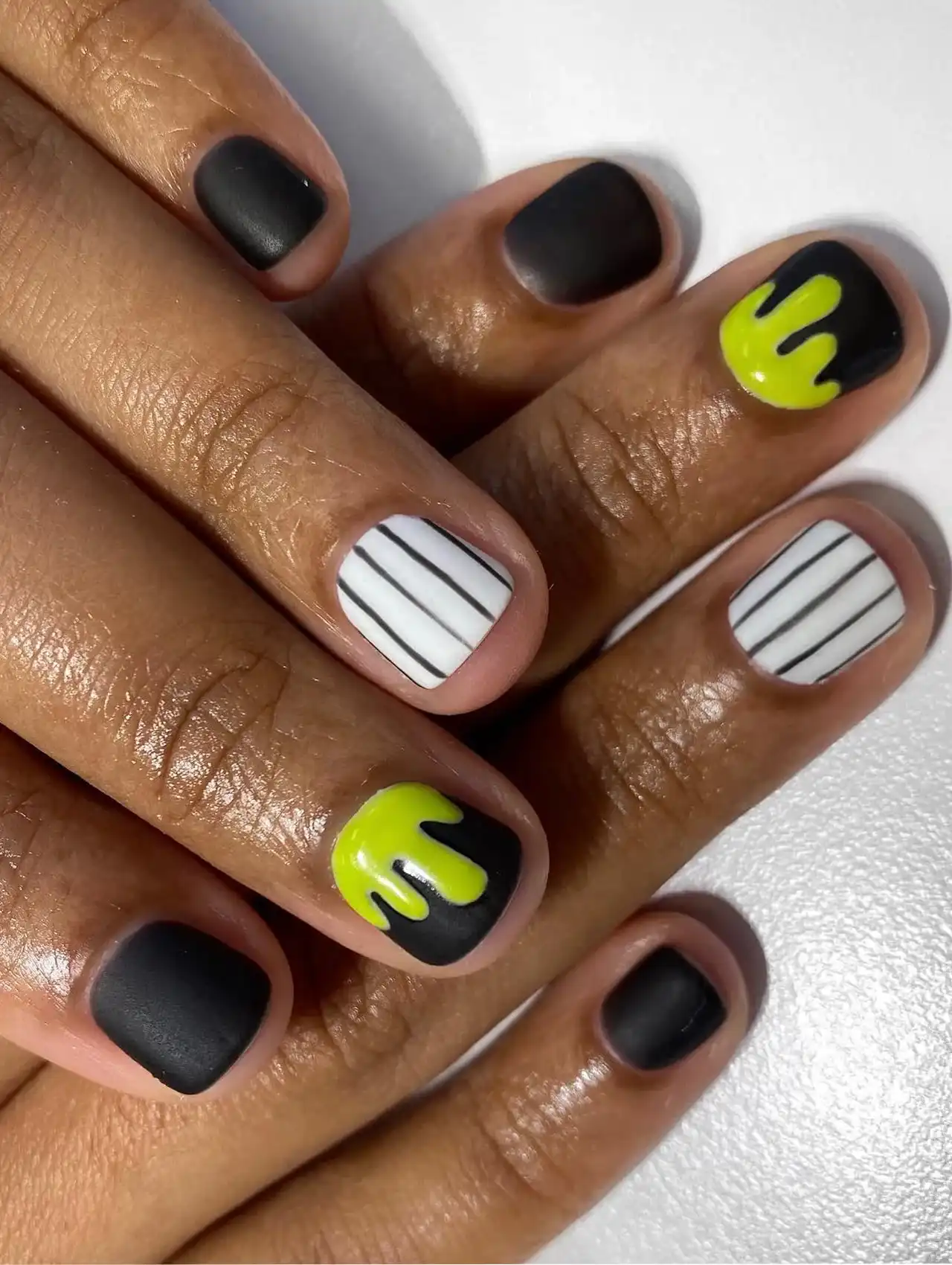 Minimalistic Halloween nails with matte black polish, neon green slime drips, and black-and-white stripes.