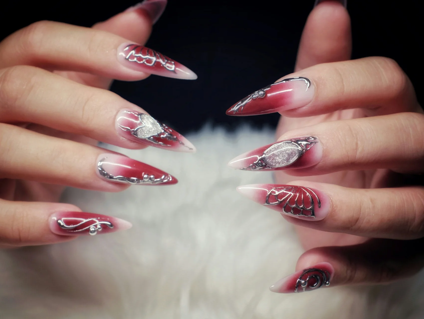 Long stiletto nails with burgundy aura gradient and 3D silver chrome hearts and butterfly wings, trendy Halloween nails
