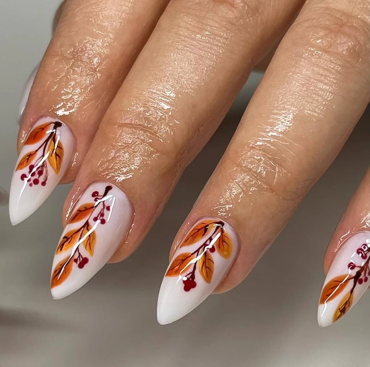 Uñas en tendencia otoño con diseño artístico de hojas naranjas y ramas con frutos rojos.