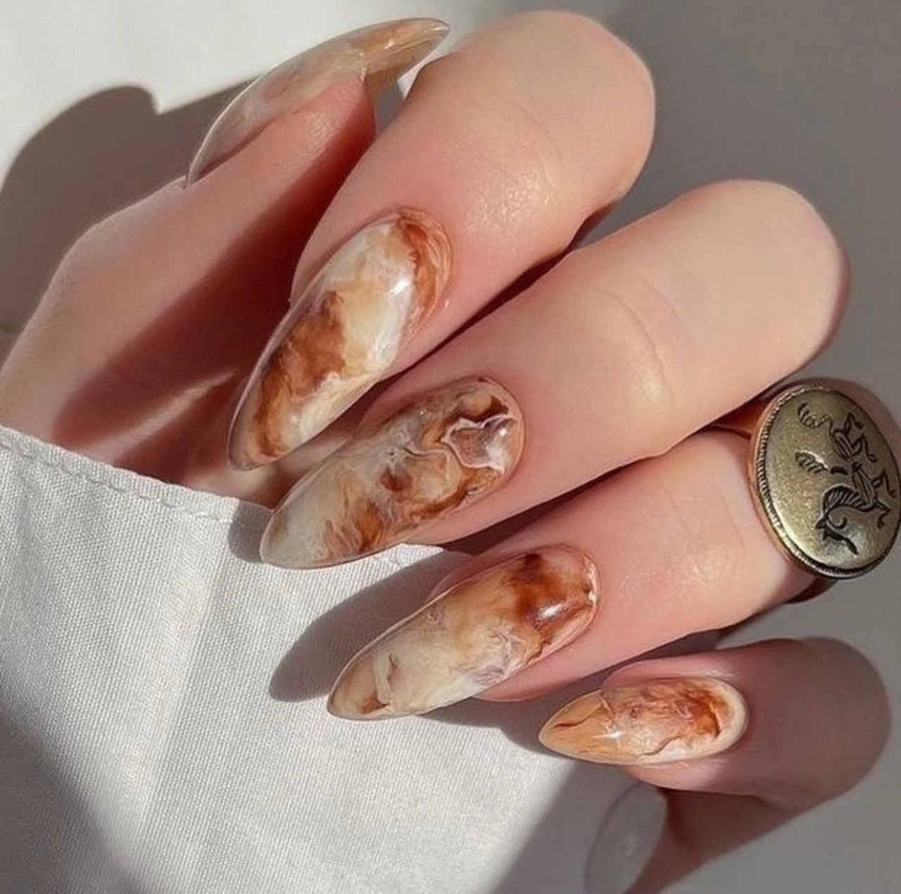 Uñas en tendencia otoño estilo latte de caramelo con efecto marmoleado en tonos cálidos.