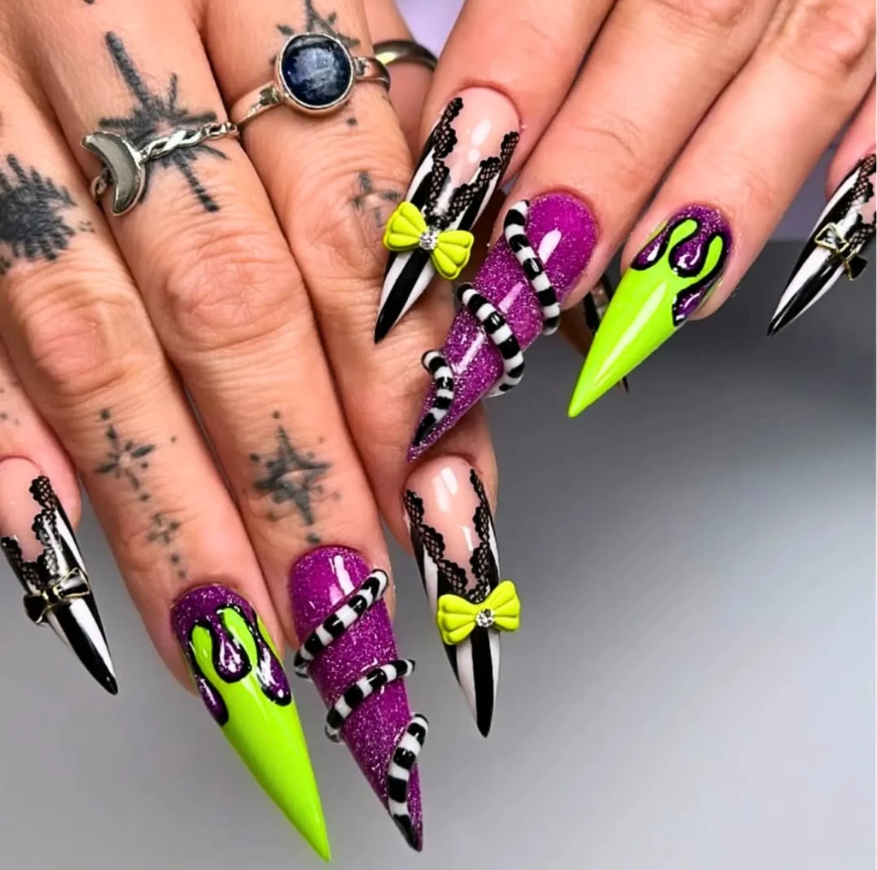Diseño de uñas elegantes y sencillas estilo Beetlejuice con tonos neón, negro, morado y rayas en punta stiletto.
