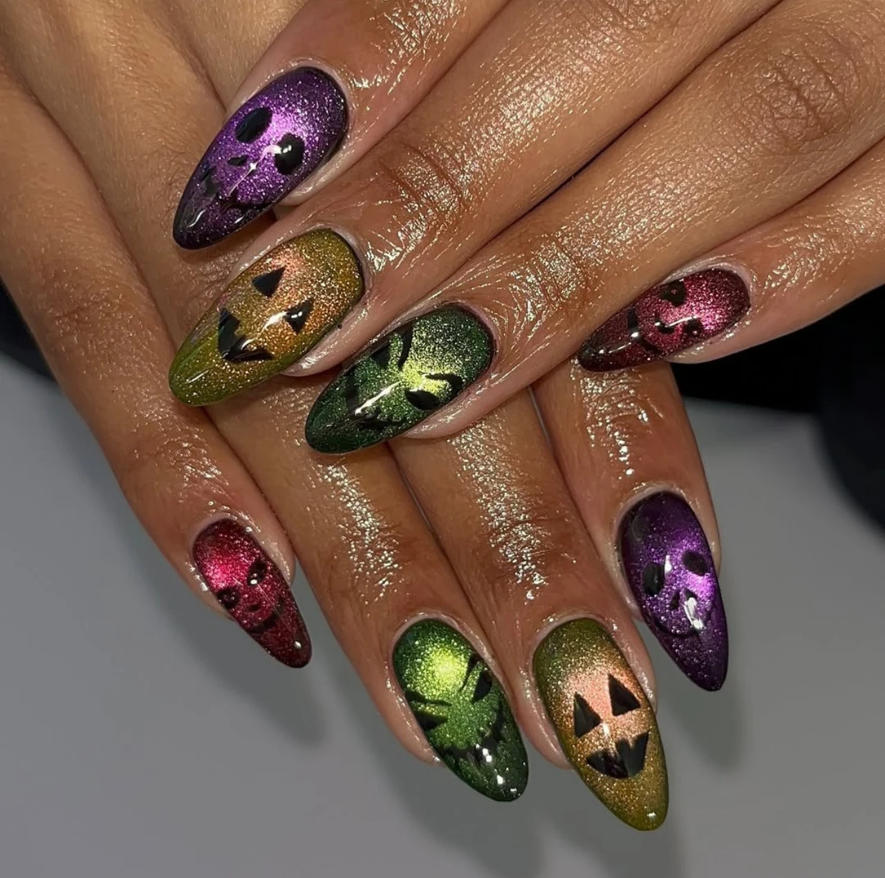 Diseño de uñas elegantes y sencillas con siluetas de gato negro sobre base metálica multicolor para Halloween.