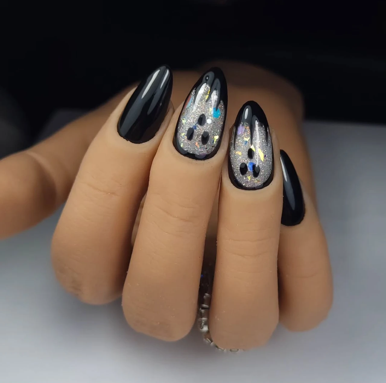 Diseño de uñas elegantes y sencillas con fantasmas en glitter sobre fondo negro.