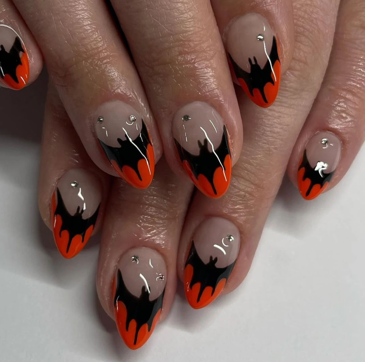 Diseño de uñas elegantes y sencillas estilo francesas con murciélagos en negro y naranja para Halloween.