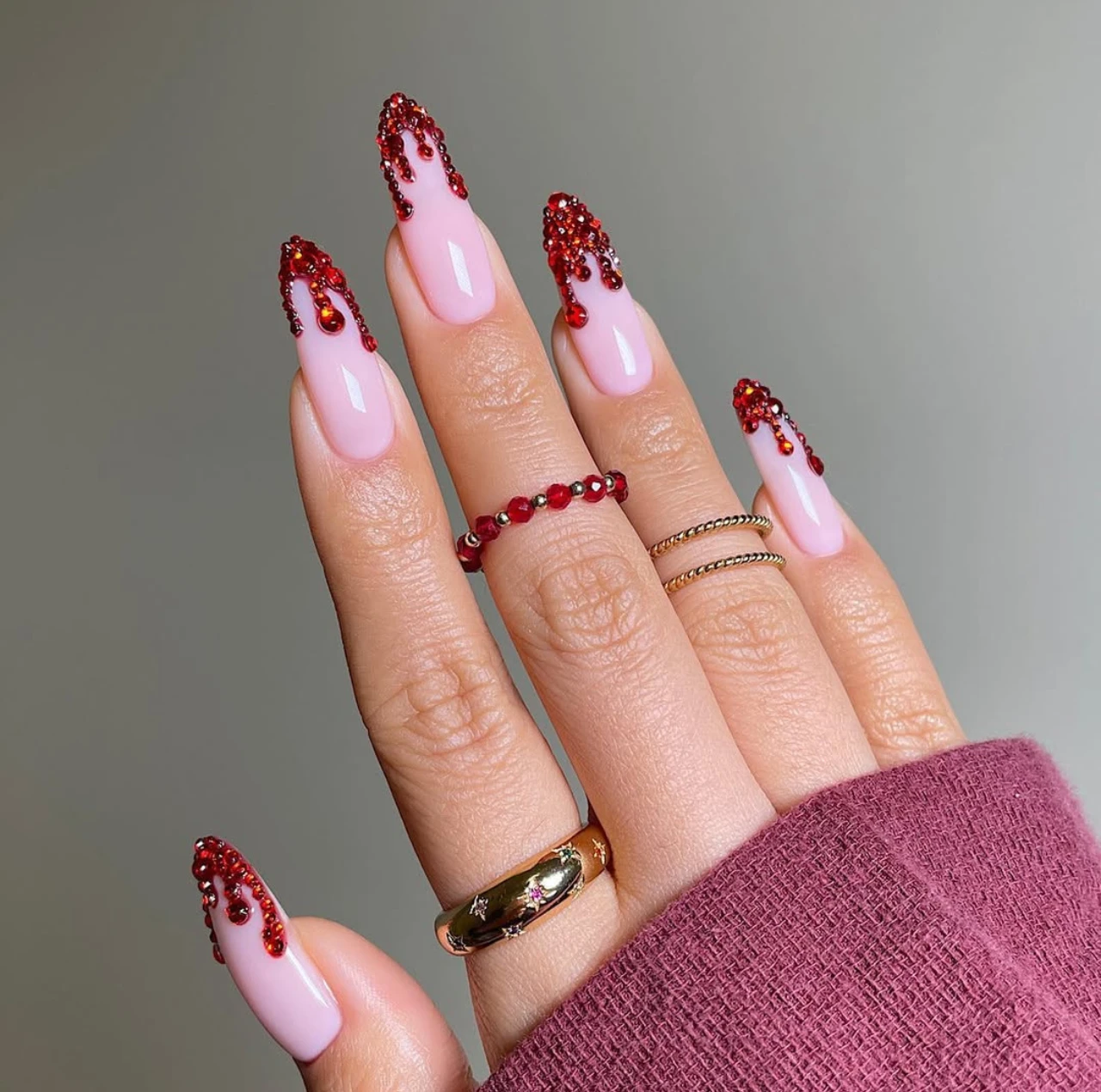 Diseño de uñas elegantes y sencillas con efecto sangriento usando pedrería roja sobre base rosa.
