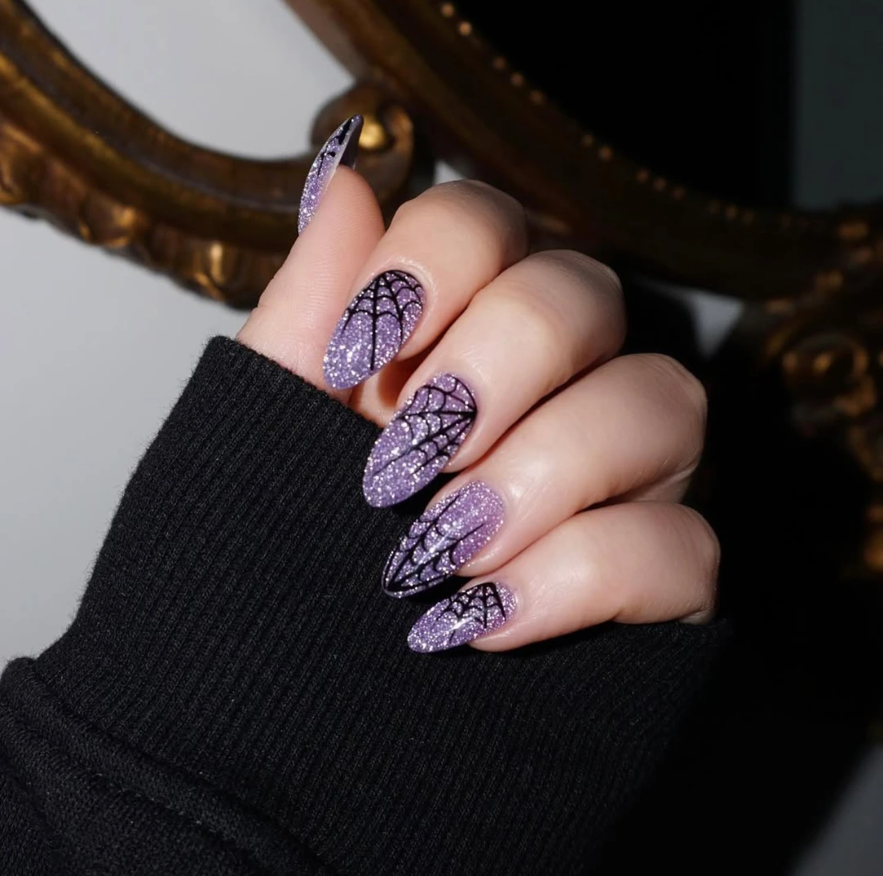 Diseño de uñas elegantes y sencillas con glitter morado y telarañas negras, ideal para Halloween.