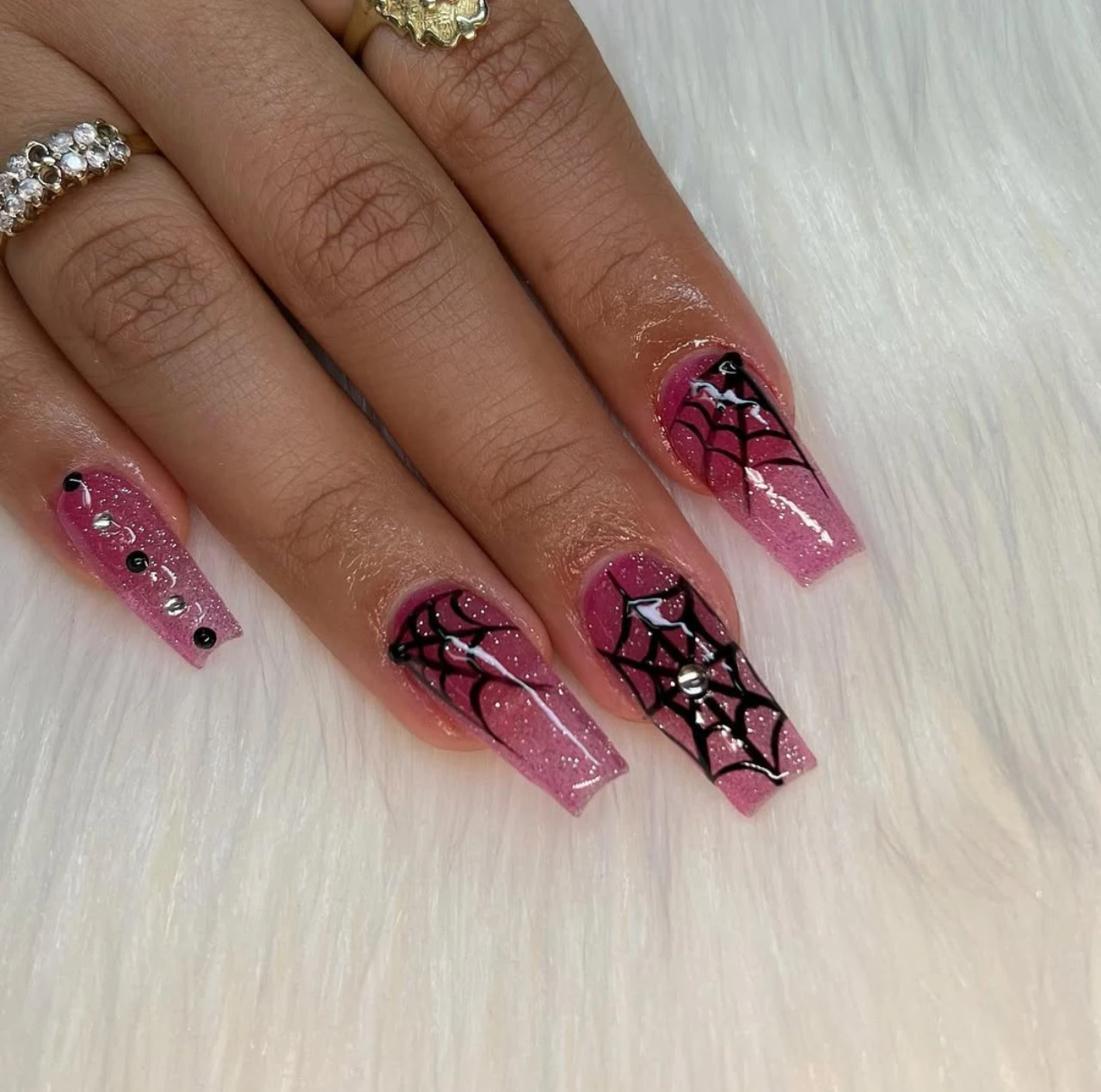 Diseño de uñas elegantes y sencillas con telarañas negras sobre base rosa chic con glitter.