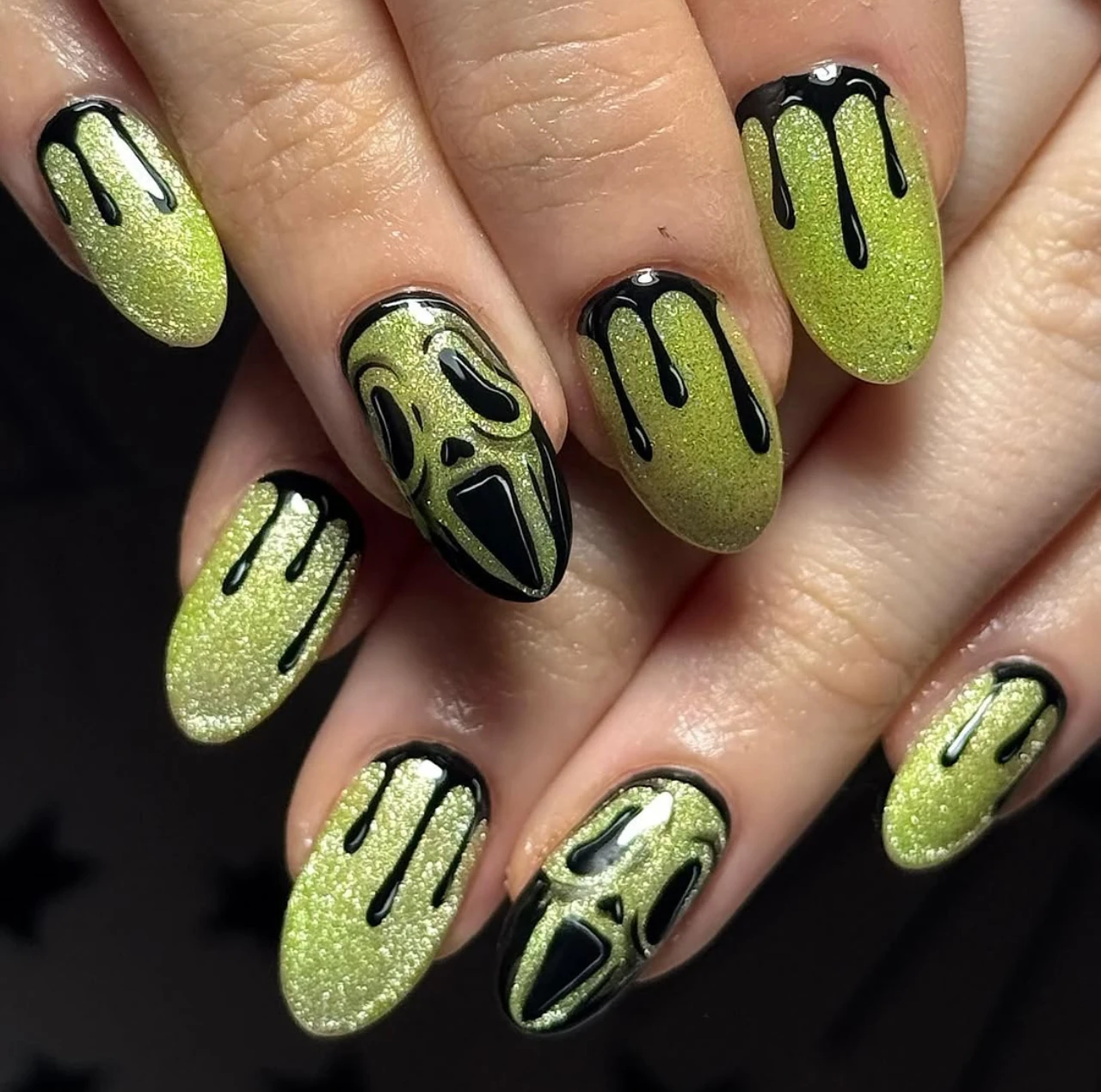 Diseño de uñas elegantes y sencillas verdes con glitter y rostros negros tipo gato o scream para Halloween.