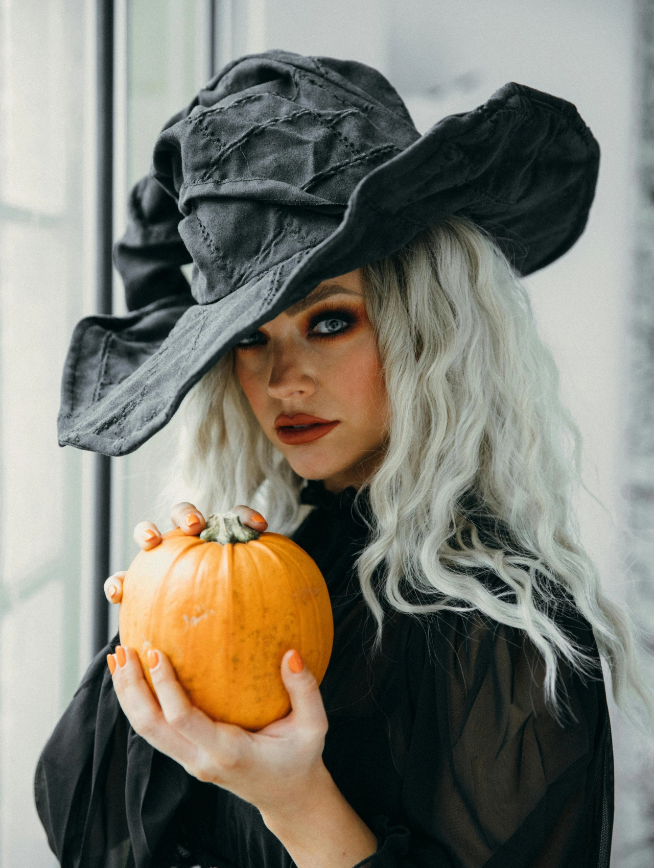 Maquillaje de bruja con cabello platinado, ojos ahumados y sombrero grande para Halloween.