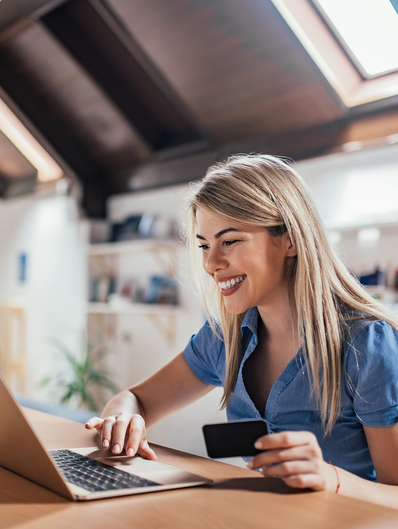 Mujer joven sonriendo mientras compra en línea con su tarjeta, aprovechando ofertas y descuentos de Black Friday Sales en su laptop