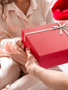 Mujer en pijama recibiendo una caja de regalo roja — ideas de regalos de Navidad para mujeres.