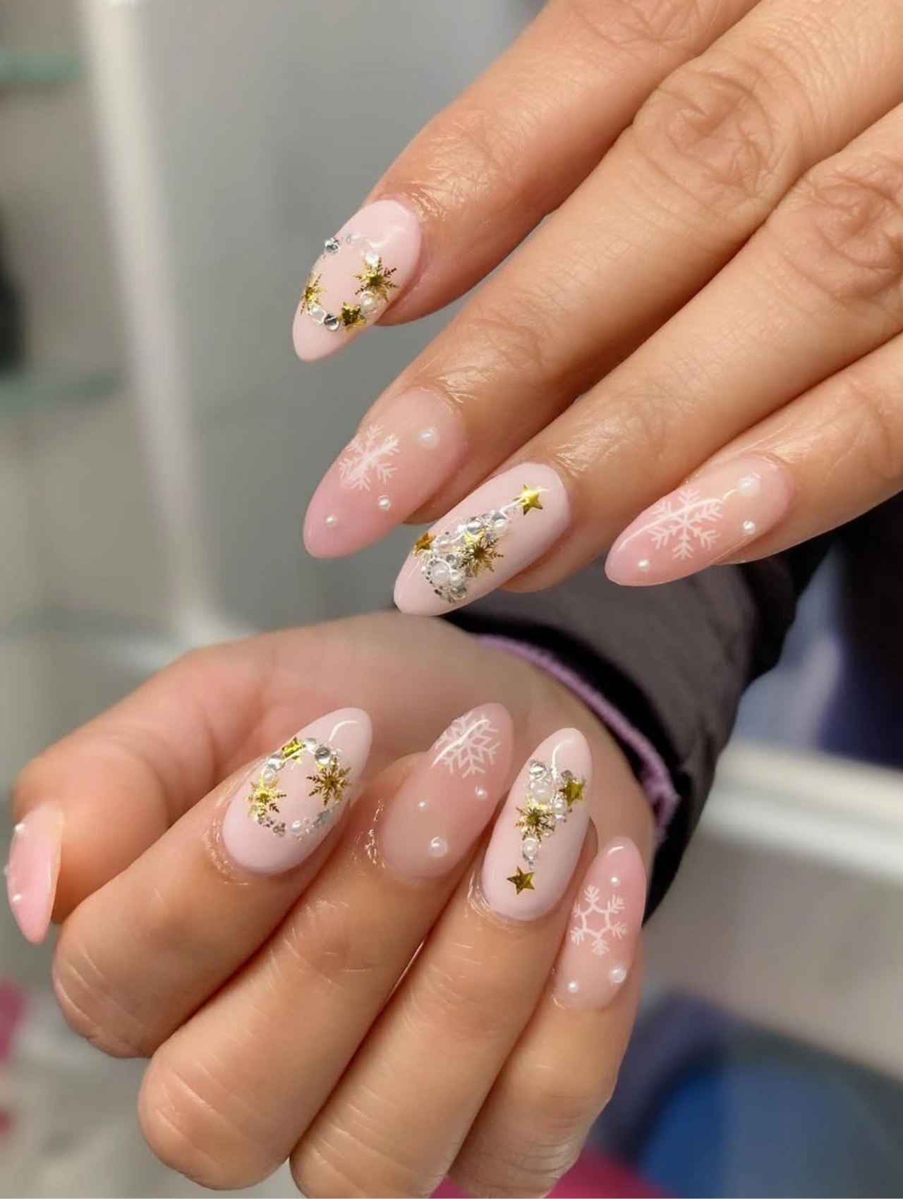 Diseños de uñas para invierno con base rosada, copos de nieve y estrellas doradas