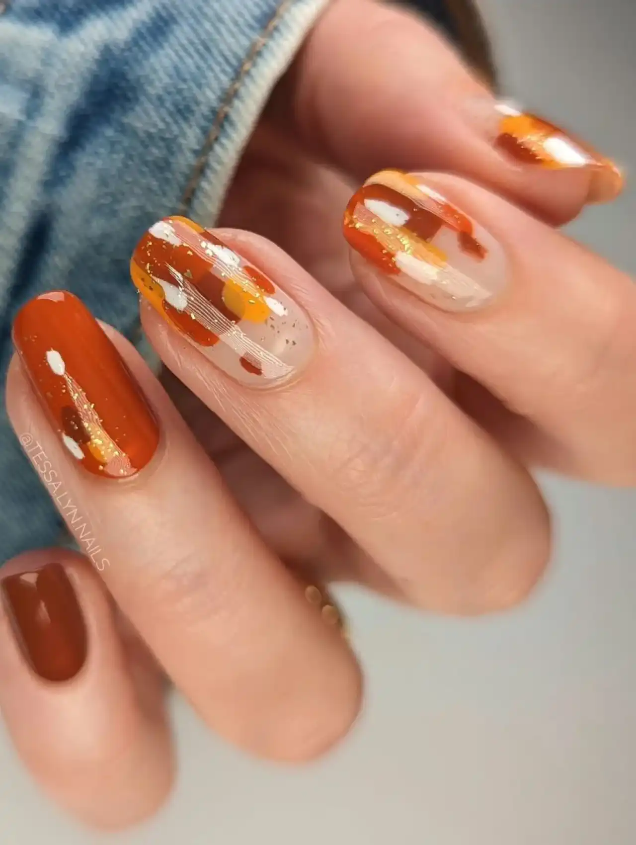 Abstract orange and brown Thanksgiving nails with gold foil accents and autumn brushstroke design