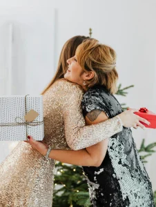 Dos mujeres abrazándose con regalos en la mano, representando alegría y unión, cosas para pedir en Navidad.