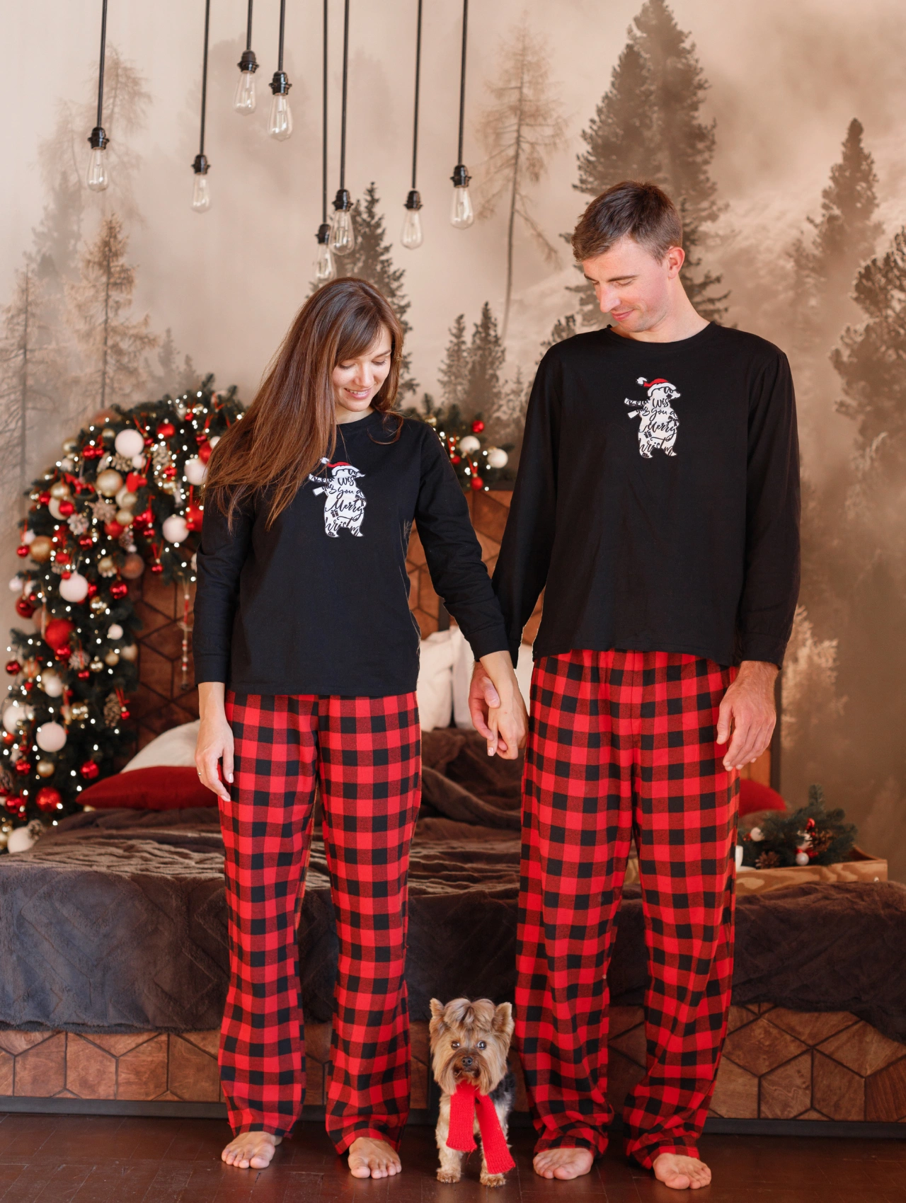 Pareja con pijamas de Navidad a cuadros rojos y negros junto a su perro, representando comodidad y estilo en las fiestas.
