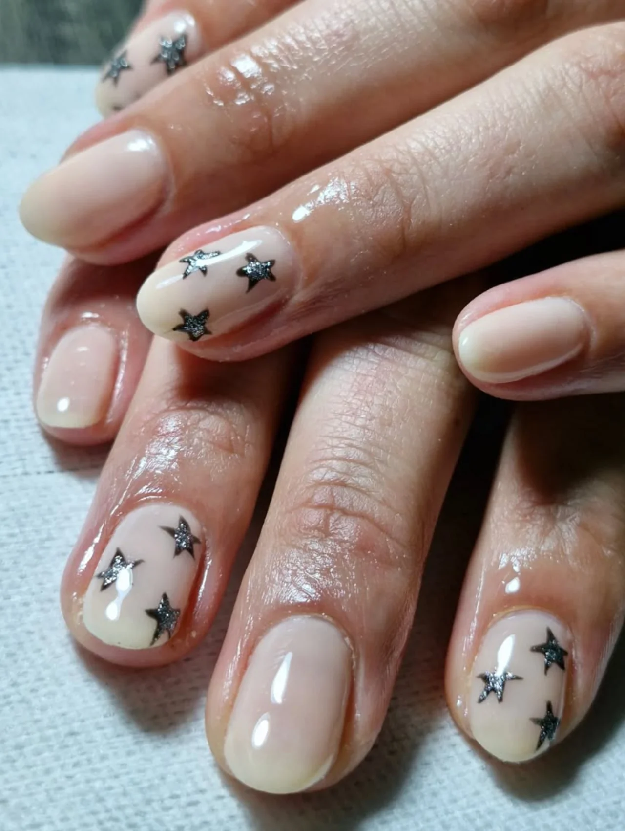 Diseño de uñas para invierno con esmalte nude y estrellas negras decorativas