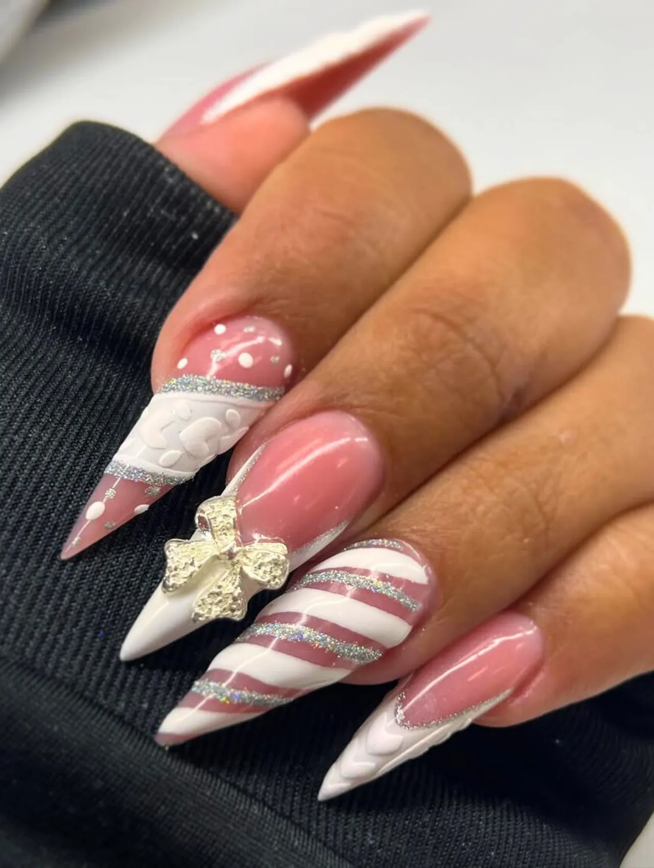 Diseño de uñas para invierno coquette con moño dorado y rayas candy cane