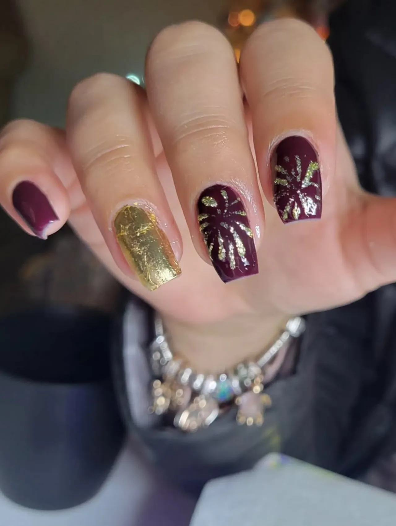 Diseño de uñas para invierno con fuegos artificiales en dorado sobre base vino