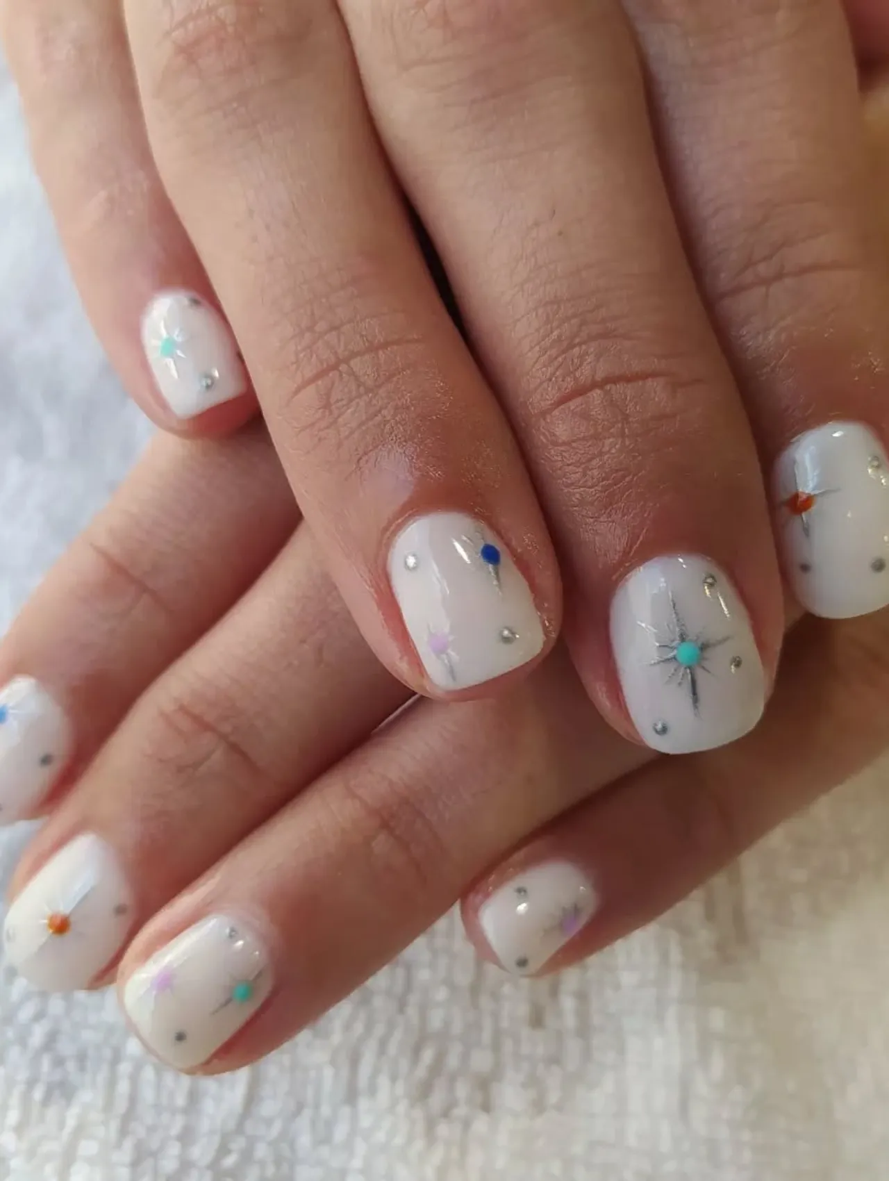 Diseños de uñas para invierno con estrellas de colores en fondo blanco