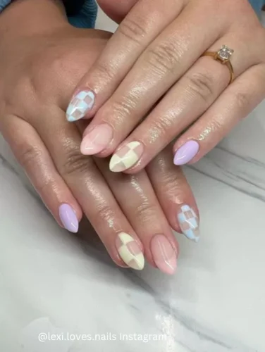 Close-up of hands displaying nails with a pastel checkerboard pattern combining soft shades of pink, blue, and beige.