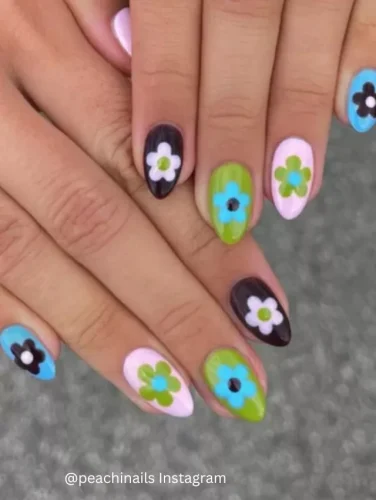 Close-up of hands displaying nails with a vibrant mix of pastel and bold colored backgrounds, each featuring a prominent flower design in contrasting shades.