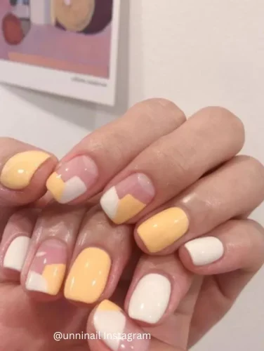 Close-up of hands displaying nails painted in a creative block pattern using shades of yellow and white.