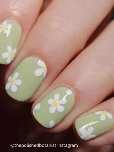 Close-up of hands displaying nails painted in a soothing olive green, each adorned with small white daisy designs.