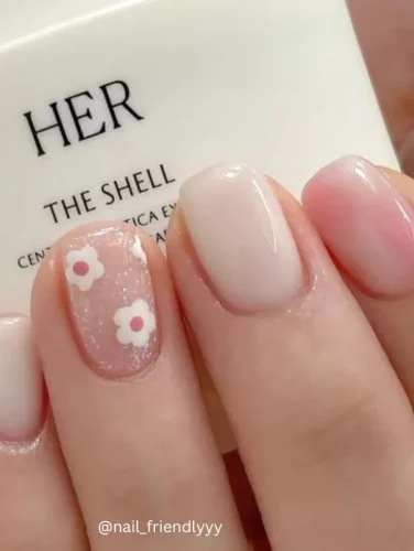 Close-up of hands displaying nails with a sheer pink base, subtly enhanced with small white flowers featuring pink centers.