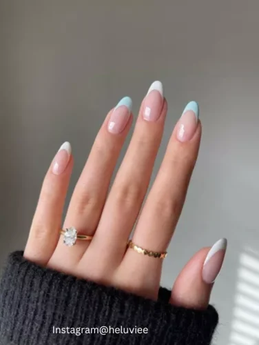 Close-up of hands displaying nails with a soft pink base, each tip delicately detailed in a pale blue shade, creating a modern take on the classic French manicure.