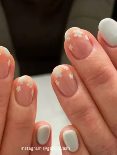 Close-up of hands displaying nails with a translucent milky pink base, each adorned with faint white floral designs, adding a whisper of spring.