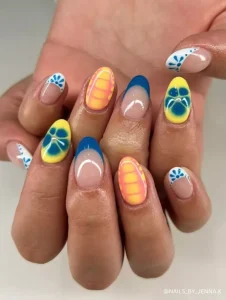 A bold and colorful manicure featuring blue French tips, yellow and orange gradient floral patterns, and intricate white and blue floral accents.