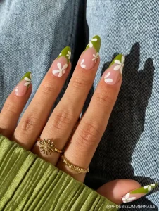 A fresh and stylish manicure featuring green French tips adorned with delicate white daisy flowers, each accented with a small rhinestone center.