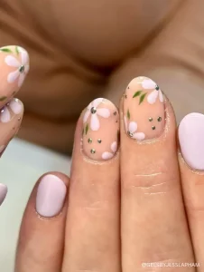 A delicate and feminine nail design featuring soft pink daisy flowers, green leaves, and subtle rhinestone accents for an elegant touch.