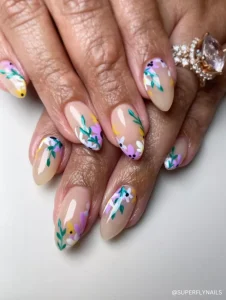 A dreamy, hand-painted floral nail design with pastel flowers, green leaves, and delicate details on a soft nude base, perfect for spring.