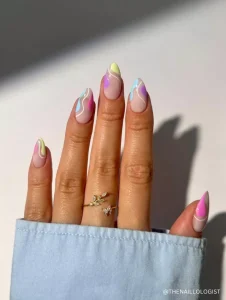 A stylish pastel wavy nail design featuring soft pink, blue, yellow, and purple swirls on a nude base, creating a dreamy spring aesthetic.