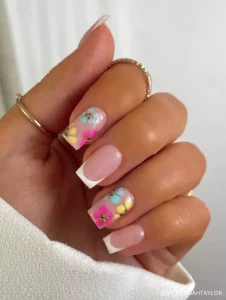 A trendy take on classic French tips featuring pastel floral accents in pink, blue, and yellow with gold embellishments.