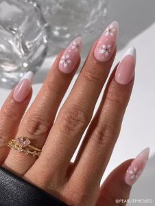 A soft pink base with white French tips and delicate white floral accents, creating an elegant and timeless spring manicure.