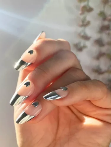 A futuristic take on Valentine's nails, this design features sleek metallic chrome French tips paired with delicate black heart accents. The nude base enhances the modern aesthetic, creating a chic contrast. Perfect for trendsetters who love a minimalist yet edgy look with a romantic touch! Ideal for stylish date nights or a bold fashion statement.