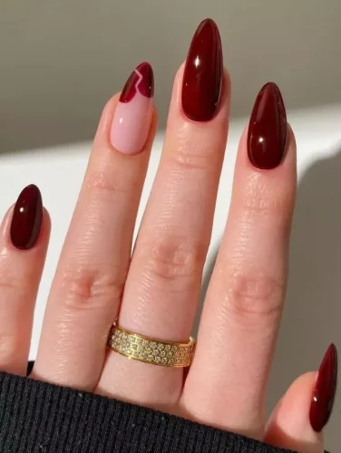 These deep burgundy nails exude elegance and mystery, perfect for a sultry Valentine's Day look. The glossy finish enhances the richness of the dark red tones, while a single accent nail with a subtle heart-shaped tip in a soft pink hue adds a delicate romantic touch. The almond shape elongates the fingers, creating a sophisticated and polished aesthetic that pairs beautifully with gold jewelry for a luxurious feel.