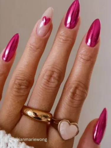 A bold and glamorous Valentine's nail design featuring ultra-shiny, metallic pink chrome nails. The look is softened with a single nude accent nail, adorned with a delicate pink heart for a romantic touch. This design exudes confidence, passion, and elegance, making it the perfect choice for those who want to make a statement this Valentine's Day. Paired with gold jewelry and a heart-shaped ring, this manicure is both trendy and timeless. 💖✨