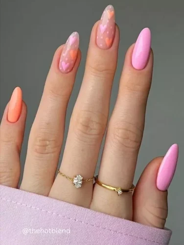 This dreamy manicure features a soft gradient of pink and peach hues, blending seamlessly for a delicate and romantic look. The accent nails showcase a translucent base adorned with tiny pastel hearts in various shades, creating a whimsical and playful effect. Perfect for Valentine’s Day or a sweet springtime aesthetic, this design embodies charm, femininity, and effortless beauty. 💕✨