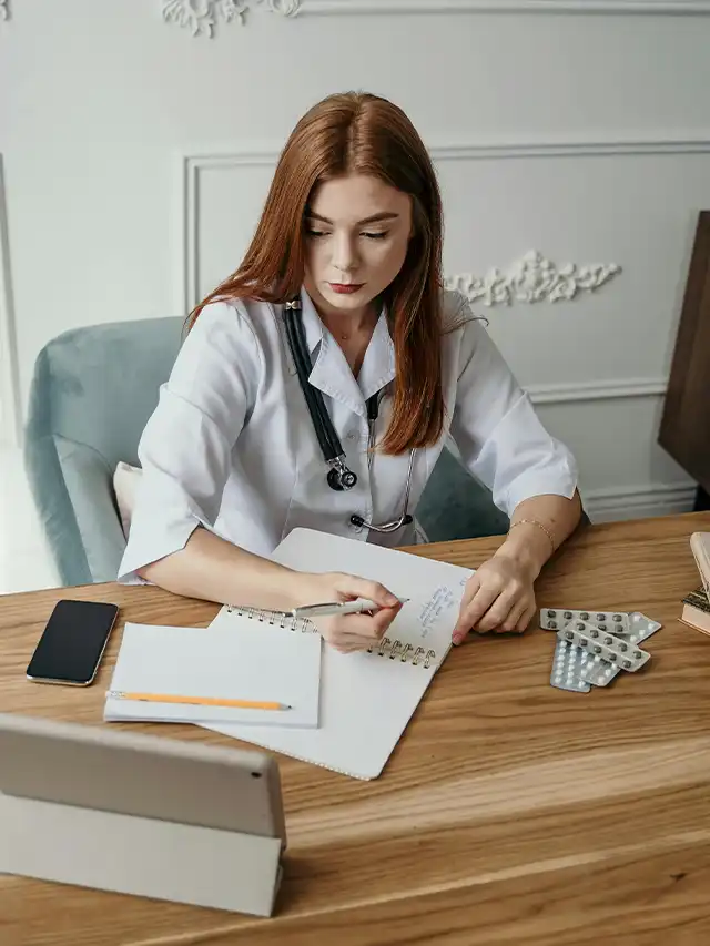 a woman in a white coat writing on a notebook