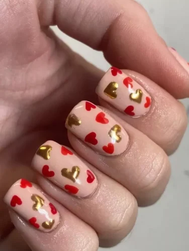 Este diseño equilibra elegantemente tonos suaves de durazno con lujosos acentos dorados, creando un aspecto que es romántico y glamuroso a la vez. Las uñas están salpicadas con una variedad de corazones rojos y dorados, meticulosamente pintados para dar una sensación de riqueza y profundidad. Perfecto para aquellos que buscan combinar el simbolismo clásico de San Valentín con un toque de opulencia, este diseño es una elección deslumbrante para cualquier ocasión celebratoria.